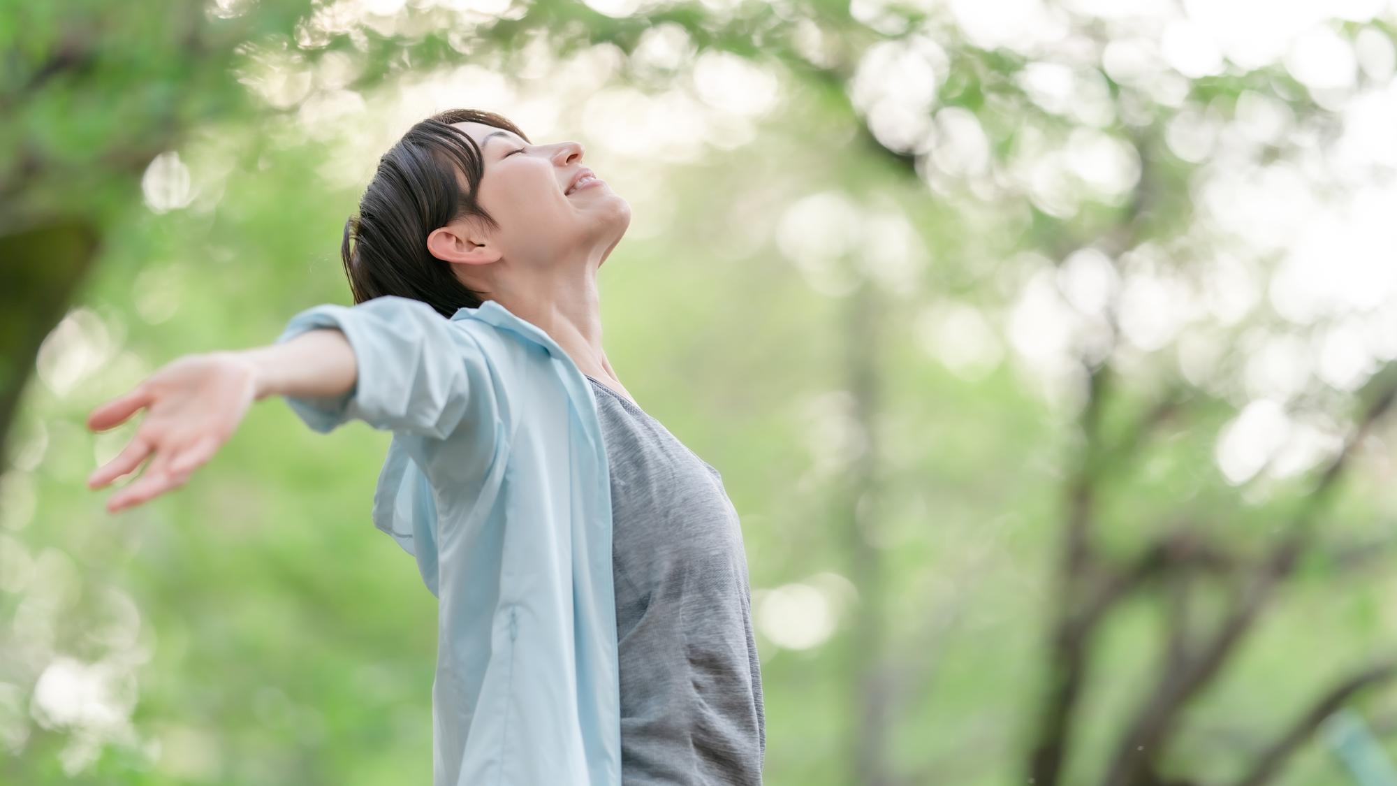 緑の中で両手を広げて深呼吸する女性
